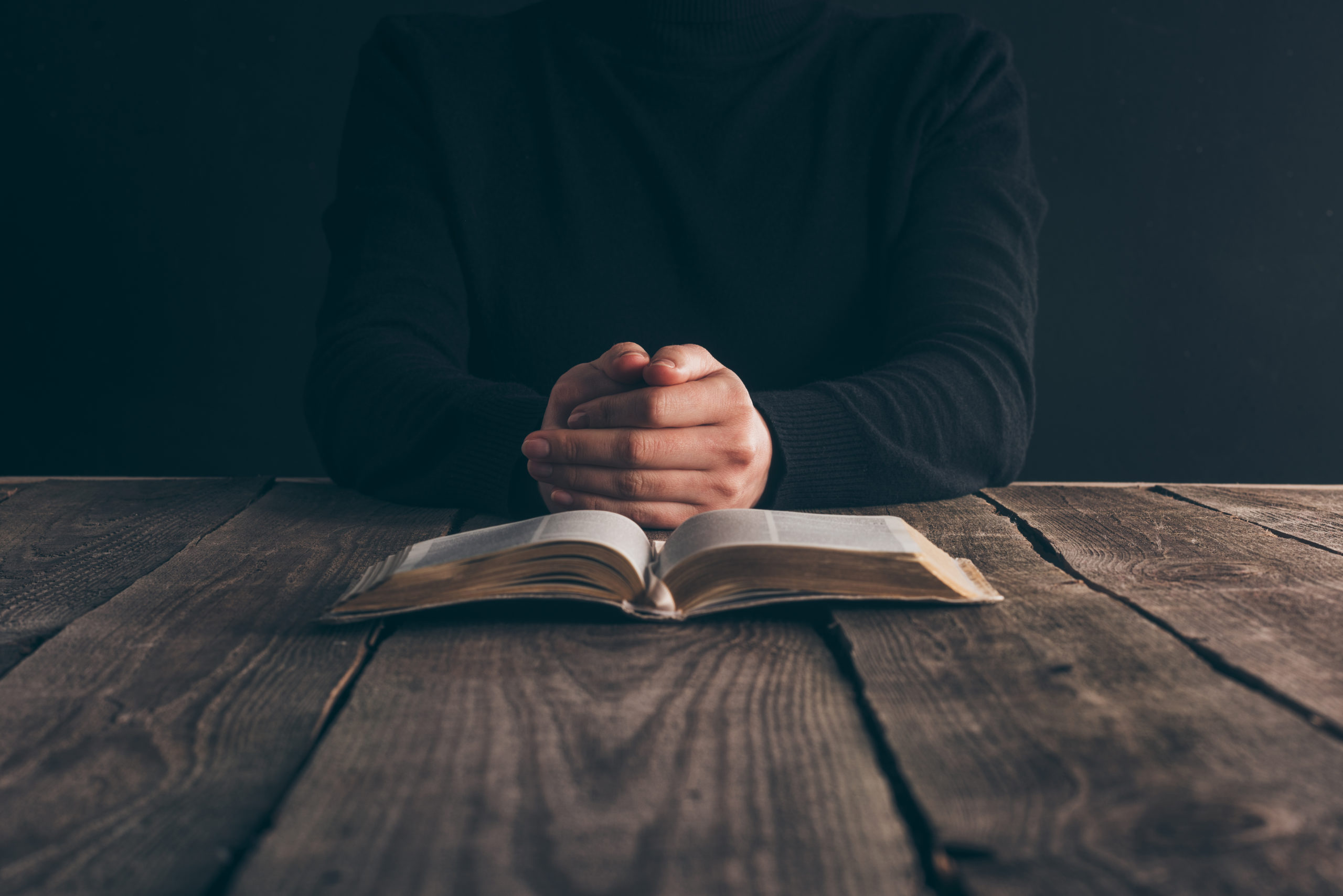 cropped image of nun sitting at table with bible and praying